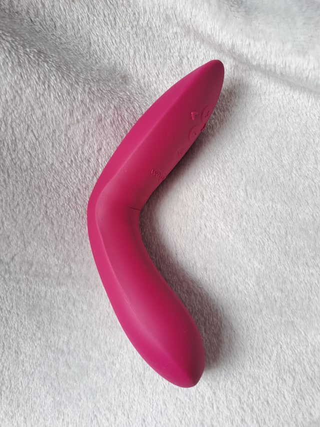A pink vibrator, the We-Vibe Rave 2, is laying on top of a white blanket.