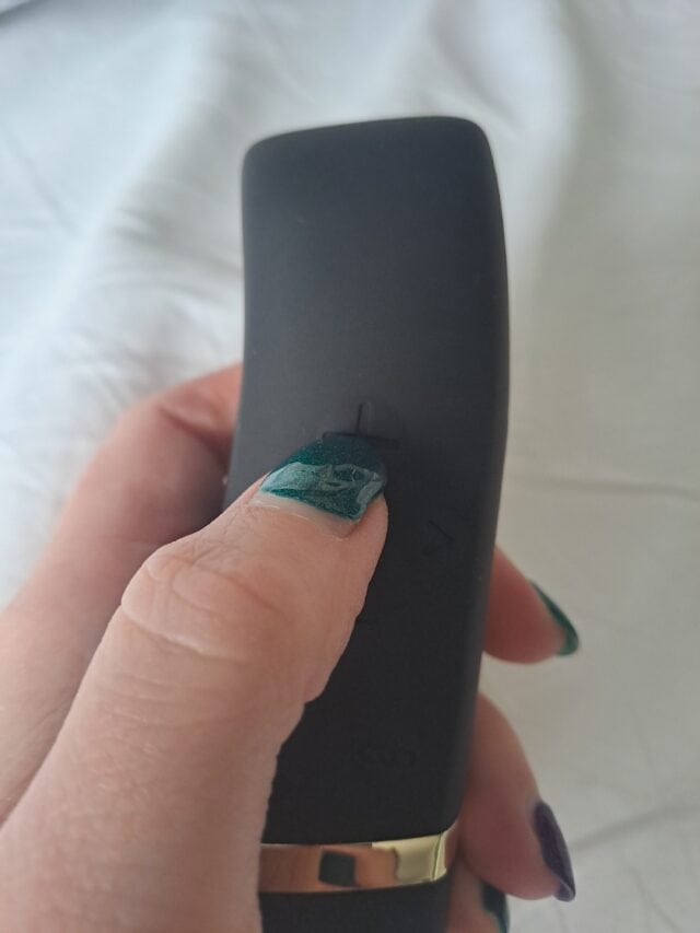 Remote control device for adult pleasure toys, black with a sleek design, held by a hand with colorful nail polish.