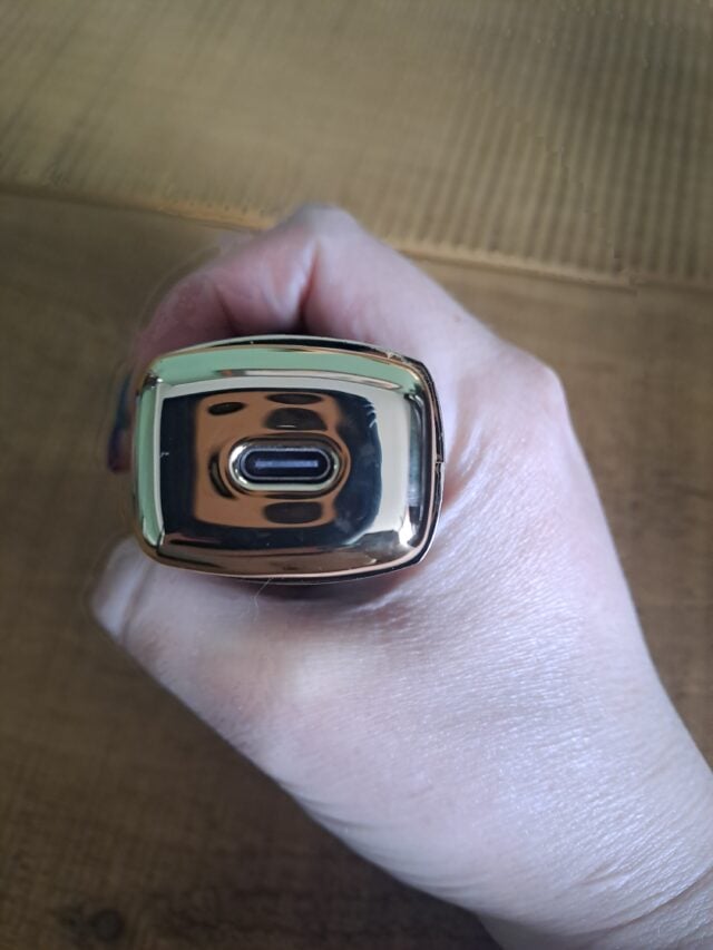Metallic vape device held in hand on a wooden surface.