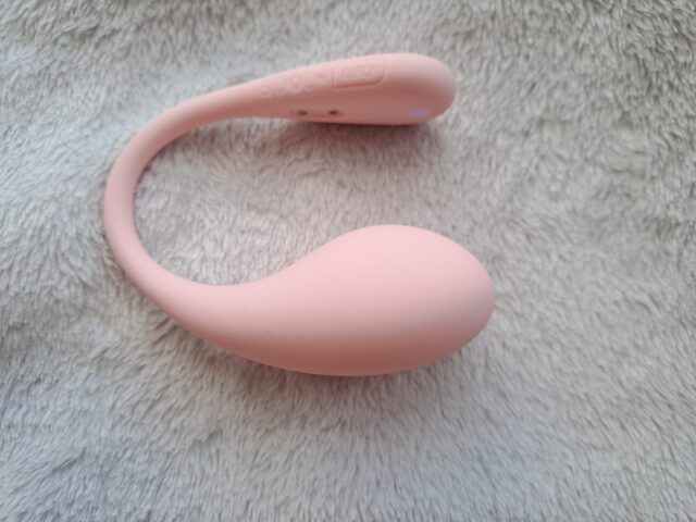 Wireless pink sex toy with remote control and multiple vibration modes on soft textured surface.