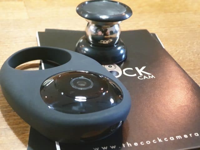 A black camera on a table, next to a book, being reviewed under the keywords "Cock Cam review" or "CockCam review".