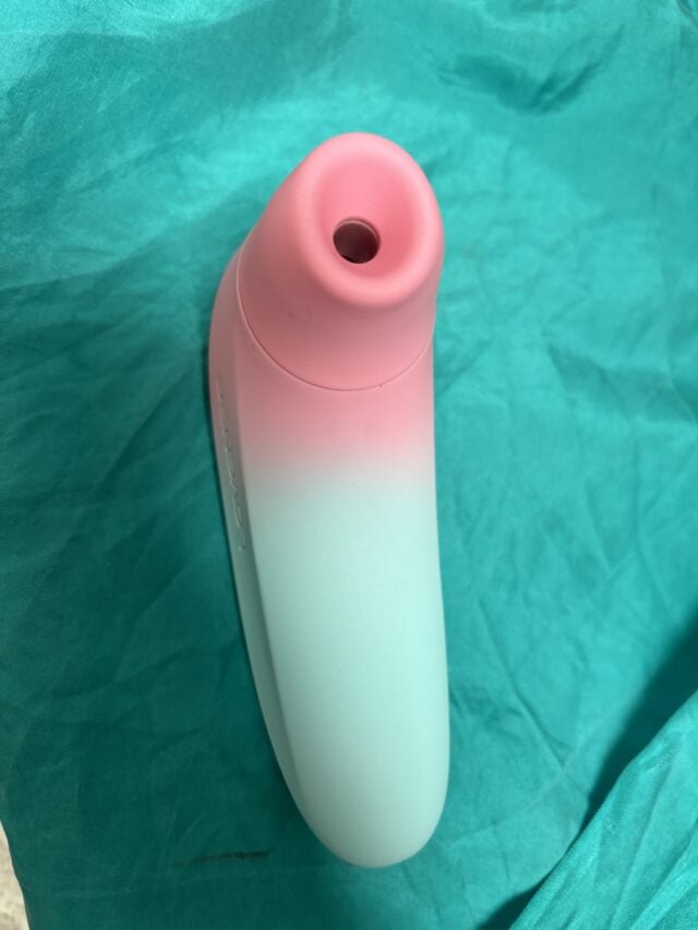 Suction-based sex toy with a pink and white gradient design on a teal fabric background, showcasing adult pleasure devices and intimate wellness products.