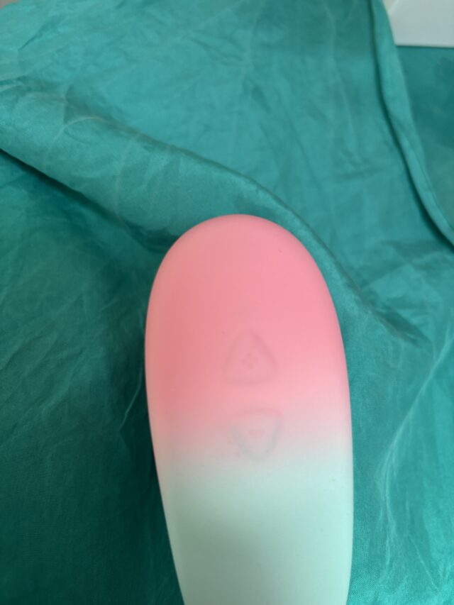 Pink sex toy on teal fabric, smooth silicone vibrator, body-safe pleasure device for adults, innovative sextech product featured on sextechguide.com, wearable intimate wellness device for enhanced pleasure.