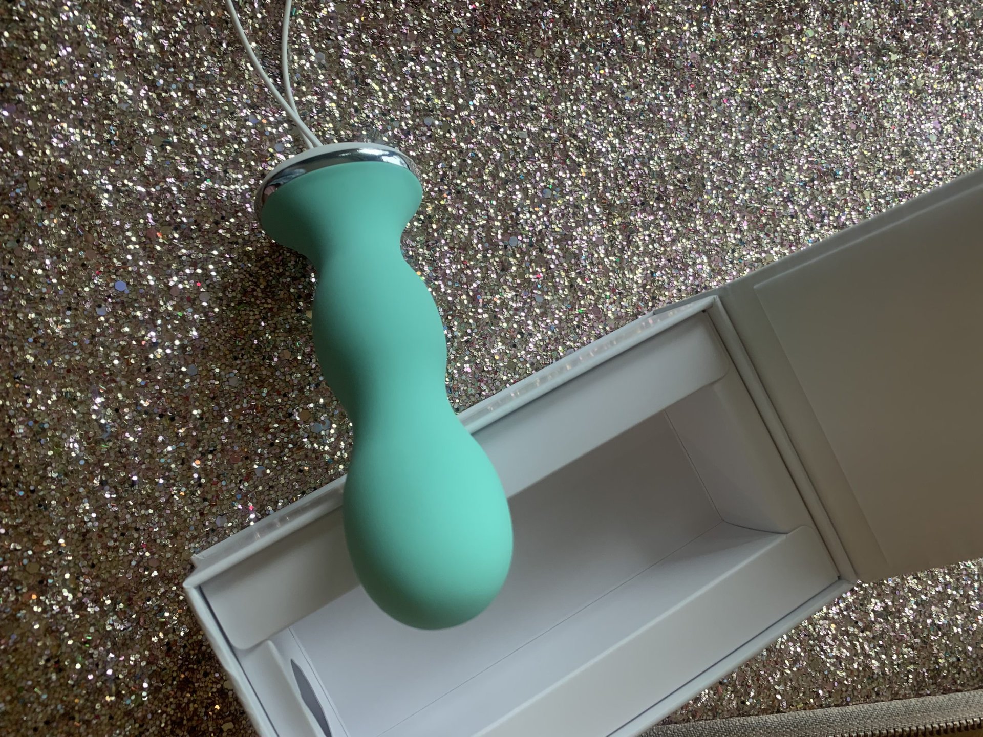 A teal Perifit kegel exerciser in a box on a glittery surface.