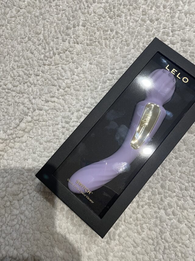 Purple dual-action sex toy with vibrating and wand features, packaged in sleek black box with clear window for display, designed for intimate pleasure and advanced stimulation.