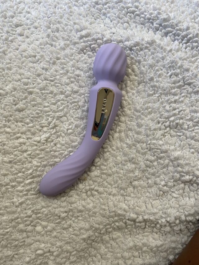 Hyper-realistic purple sex toy with curved design and gold control panel on textured white surface.