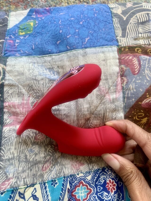 Red silicone vibrator with a curved design for G-spot stimulation lying on colorful patterned quilt.