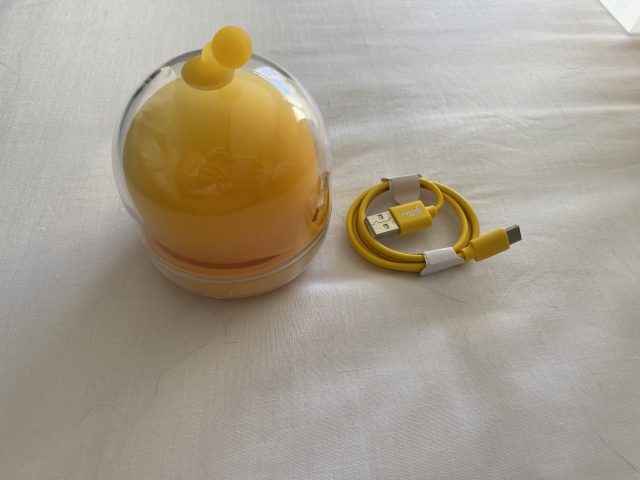 Power bank with a yellow capsule-shaped object inside, and a yellow USB charging cable on a white surface.