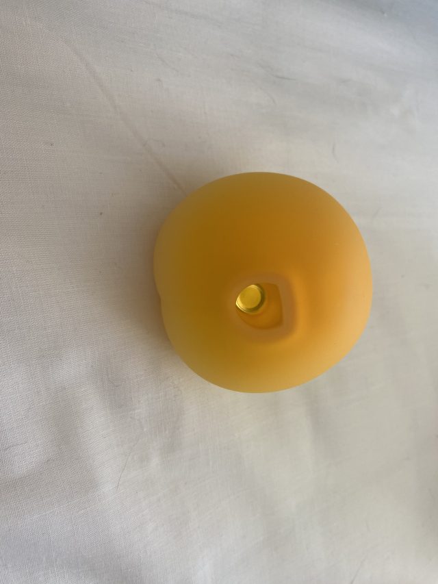 Spherical yellow silicone object with a central hole, possibly a candle or a decorative item, on a white fabric surface.