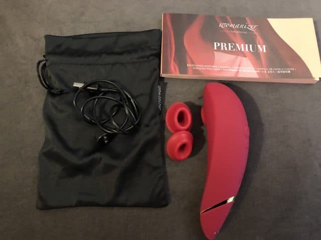 A Womanizer Premium vibrator accompanied by earphones and a bag.
