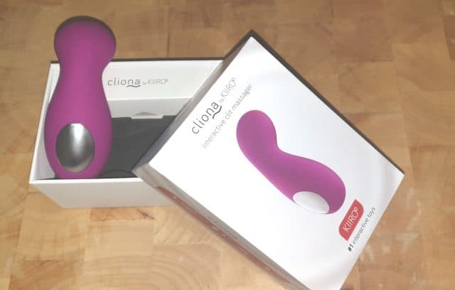 A Kiiroo Cliona, a purple vibrator, in a box on top of a table.