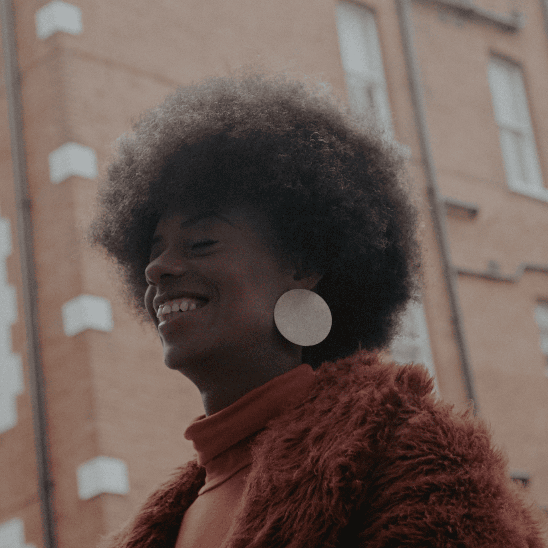 Black woman smiling outdoors wearing stylish earrings and a fur coat for sextech lifestyle and empowerment themed photo.