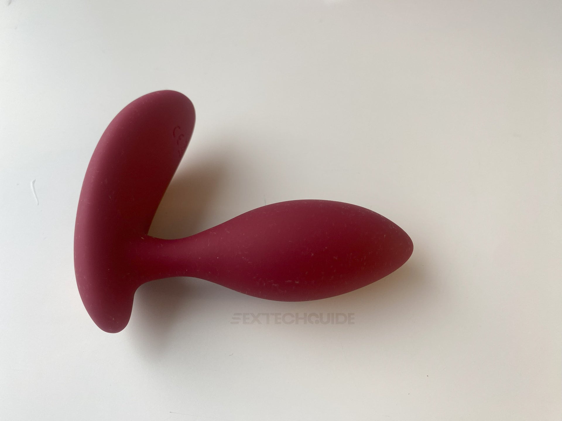 A red sex toy, specifically designed for anal pleasure, on a smooth white surface.