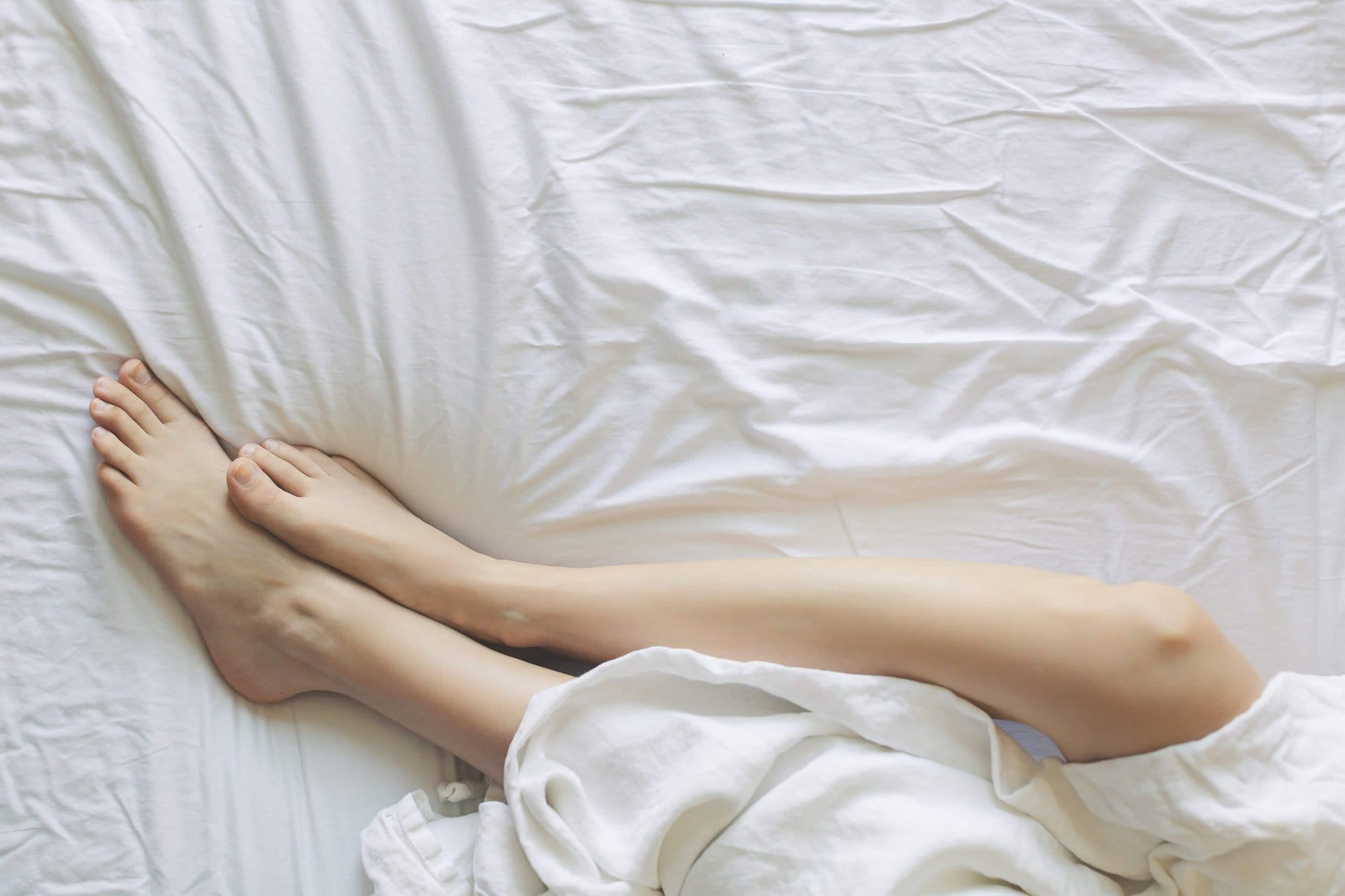A woman's long-distance love expressed through her feet resting on a white bed.