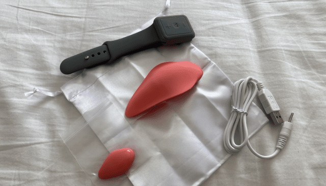 A red sex toy, the Clandestine Companion panty vibe, is discreetly resting on a bed.