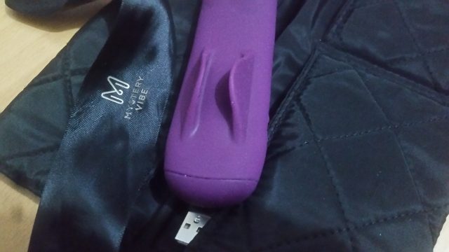 A purple vibrator is sitting on top of a black bag in this MysteryVibe Crescendo review.