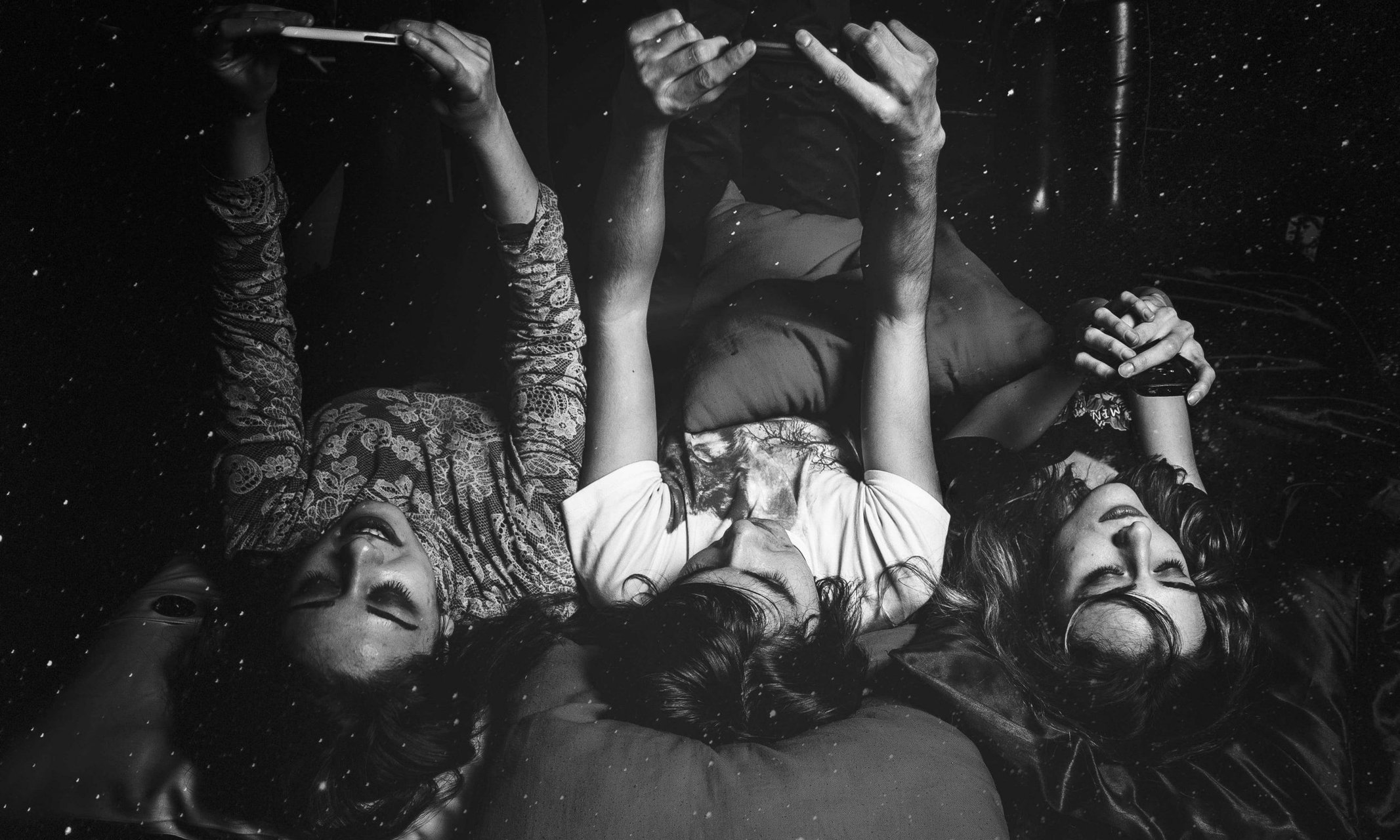 A monochrome photo depicts a gathering of individuals reclining on a bed, highlighting the detrimental impact of phones on relationships and personal responsibility.