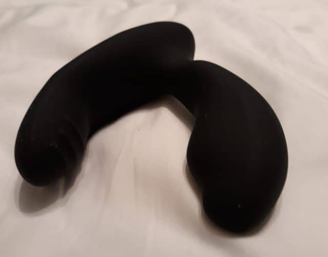 A Desire Prostate Vibe, a black sex toy, sitting on top of a bed.