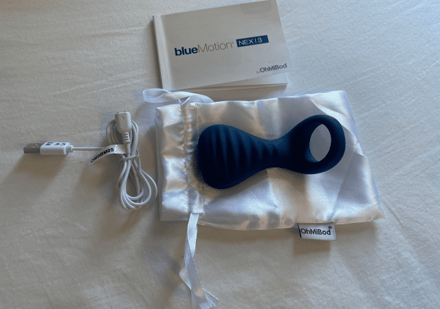 A blue OhMiBod Nex 3 vibrator is discreetly placed on a bed.