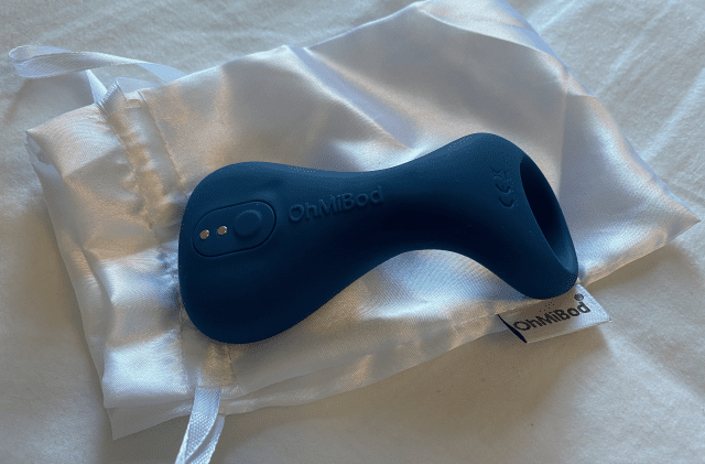 A blue OhMiBod Nex 3 sex toy is resting on a white pillow.