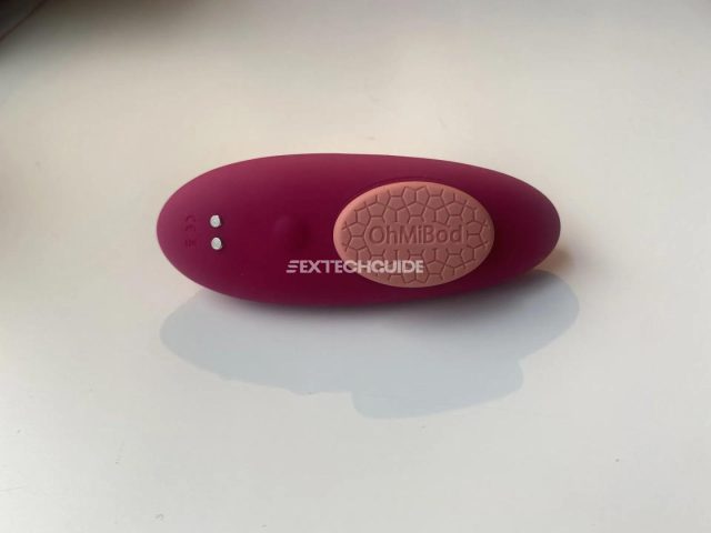 A foxy pink and brown vibrator, known as OhMiBod, rests on top of a pristine white surface.