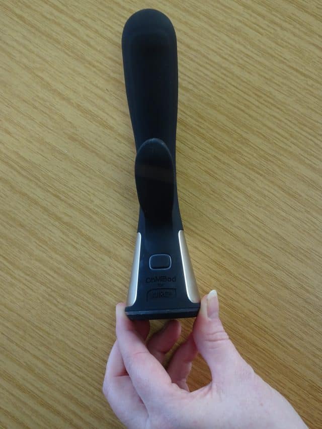 A person's hand holding a black and white remote control for an OhMiBod Fuse.