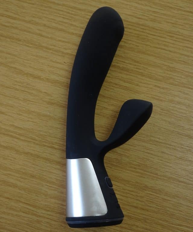 A black and silver sex toy on a wooden table reviewed as an OhMiBod Fuse.