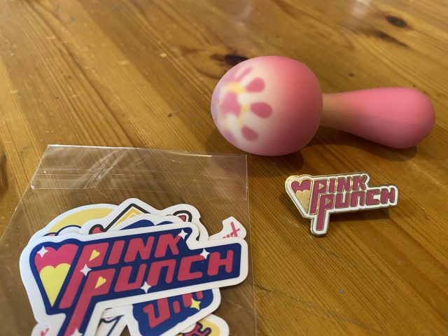 A PinkPunch Sunset Mushroom teddy bear sits next to a sticker on a table.
