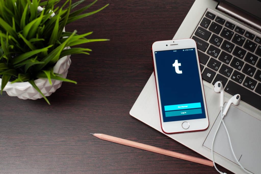 A laptop with a Tumblr app on it sits on a wooden table, as the Wordpress owner acquires Tumblr but maintains the ban on porn.