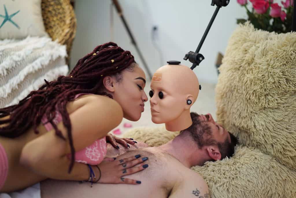 A couple engaging in surprising tech by kissing a mannequin head.